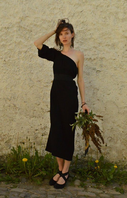 Model is wearing reversible black midi dress with one sleeve