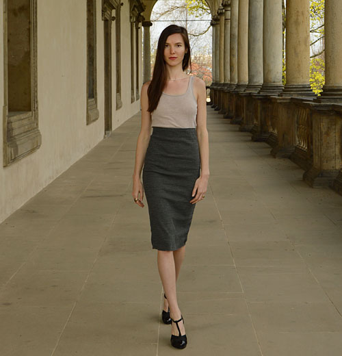 Modelka má oblečenú úzku sivú sukňu pod kolená s veľmi zvýšeným pásom a tielko krémovej farby